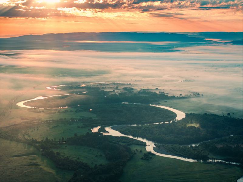 A river winding through the steppe at dawn, seen from the air